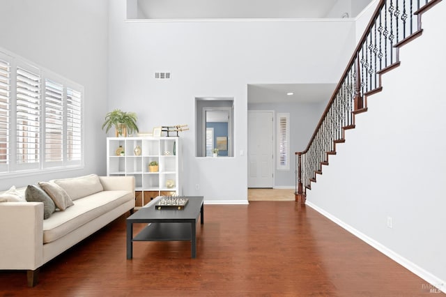 living area with stairs, visible vents, a high ceiling, and wood finished floors