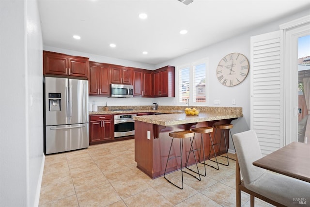kitchen featuring recessed lighting, reddish brown cabinets, a peninsula, and appliances with stainless steel finishes