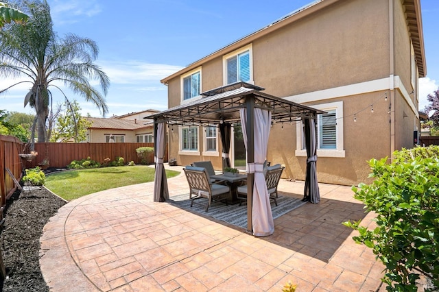 rear view of property with stucco siding, a lawn, a gazebo, a fenced backyard, and a patio area