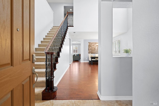 foyer with wood finished floors, stairway, baseboards, and a towering ceiling