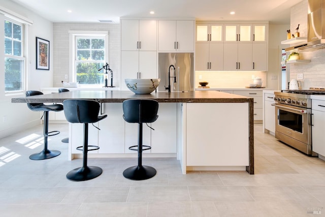 kitchen featuring high end appliances, wall chimney exhaust hood, visible vents, decorative backsplash, and recessed lighting