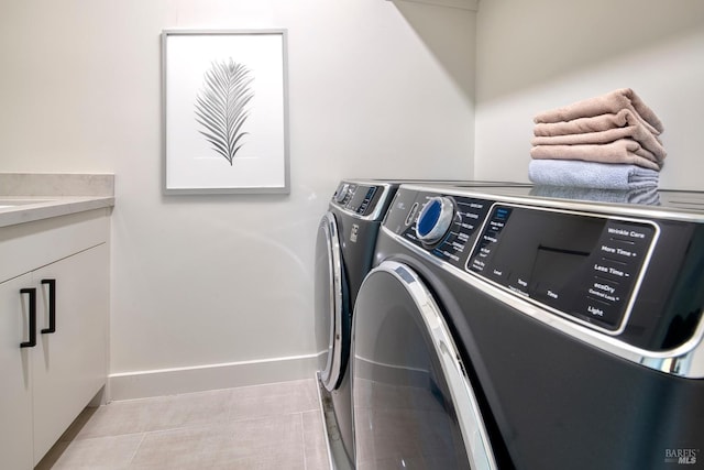 washroom with baseboards, light tile patterned floors, cabinet space, and washer and clothes dryer