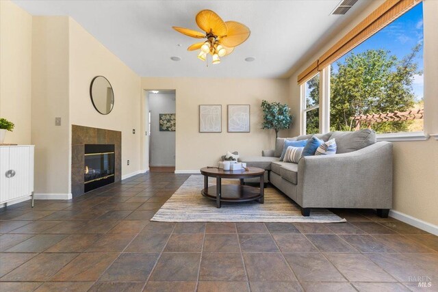 living area with ceiling fan, baseboards, a tile fireplace, and stone finish floors