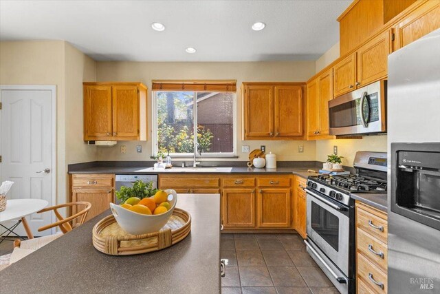 kitchen with stainless steel appliances, a sink, dark countertops, recessed lighting, and dark tile patterned flooring
