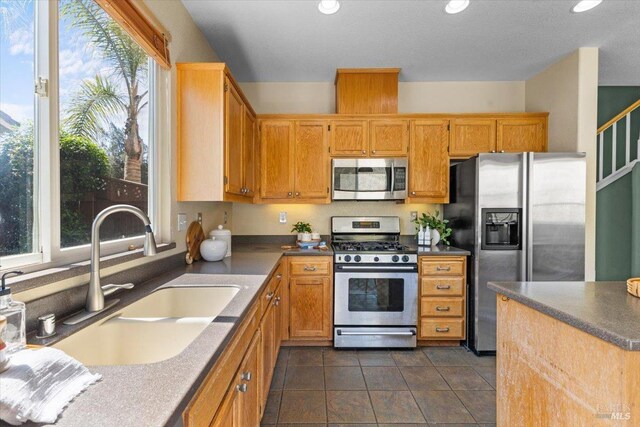 kitchen with appliances with stainless steel finishes, a sink, recessed lighting, dark tile patterned flooring, and dark countertops