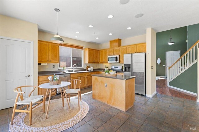 kitchen with stainless steel appliances, a sink, a center island, dark countertops, and recessed lighting