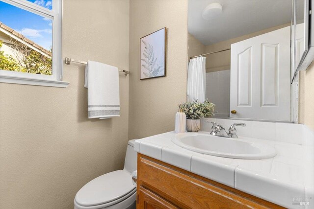 bathroom featuring toilet, vanity, a shower with curtain, and a textured wall