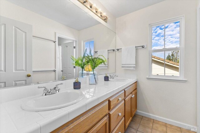 bathroom featuring baseboards, double vanity, and tile patterned floors