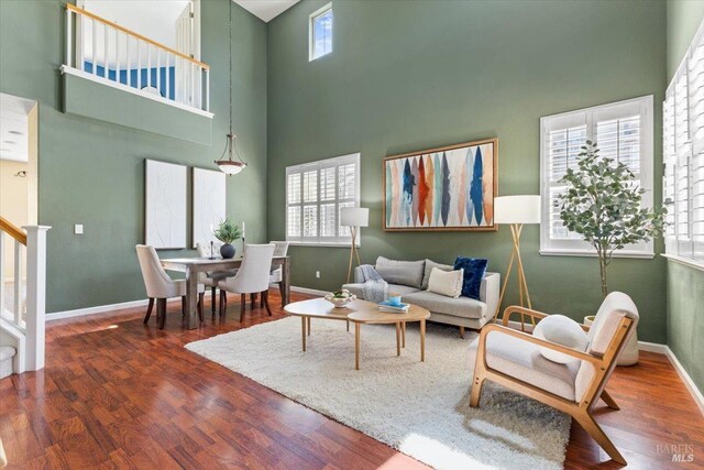 living room featuring a high ceiling, wood finished floors, baseboards, and stairway