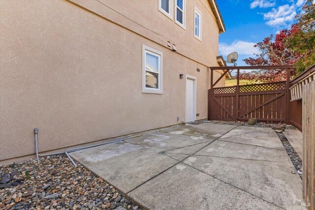 view of side of home featuring stucco siding, a gate, fence, and a patio area