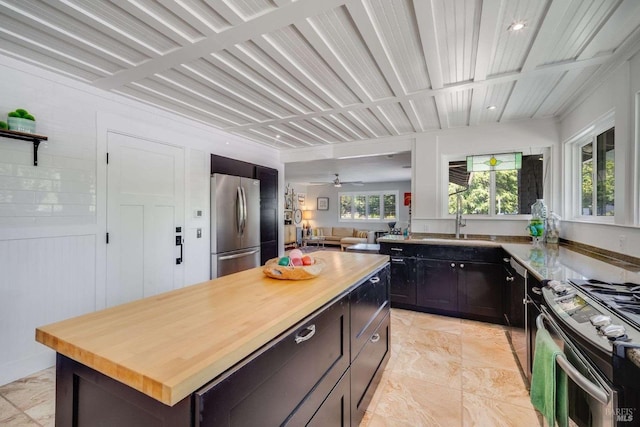 kitchen featuring a kitchen island, wooden counters, stainless steel appliances, and a sink
