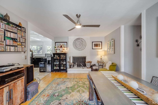 living room with light wood finished floors, a brick fireplace, and a ceiling fan