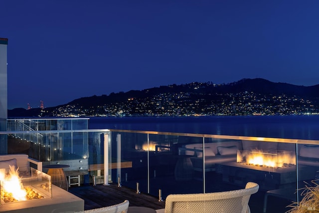 27 W Shore Rd, Belvedere, CA 94920 - balcony at twilight featuring an outdoor fire pit, a warm lit fireplace, and a mountain view