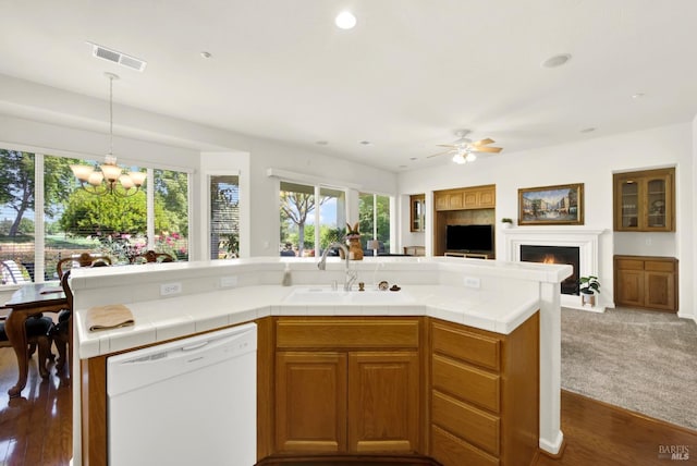 kitchen with ceiling fan with notable chandelier, a sink, visible vents, a warm lit fireplace, and white dishwasher