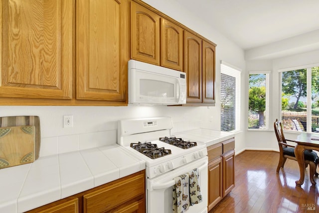 kitchen with baseboards, brown cabinetry, white appliances, dark wood finished floors, and tile counters