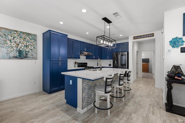 kitchen with a breakfast bar area, under cabinet range hood, light countertops, blue cabinetry, and appliances with stainless steel finishes