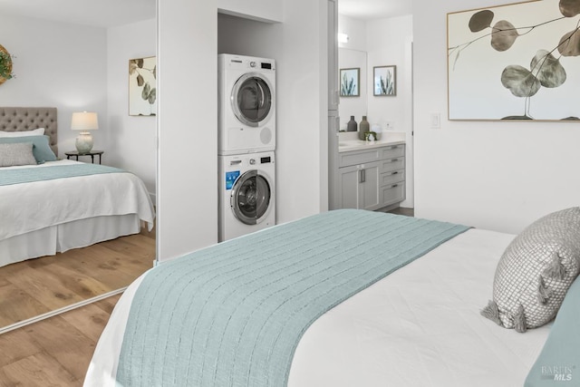 bedroom with stacked washer and dryer, ensuite bath, and wood finished floors