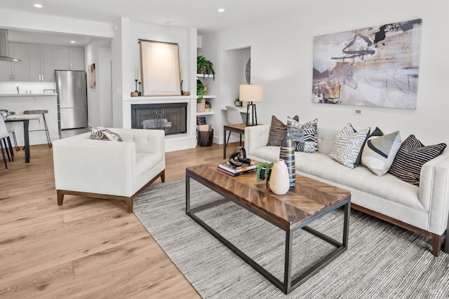 living area featuring recessed lighting, baseboards, a glass covered fireplace, and light wood-style floors