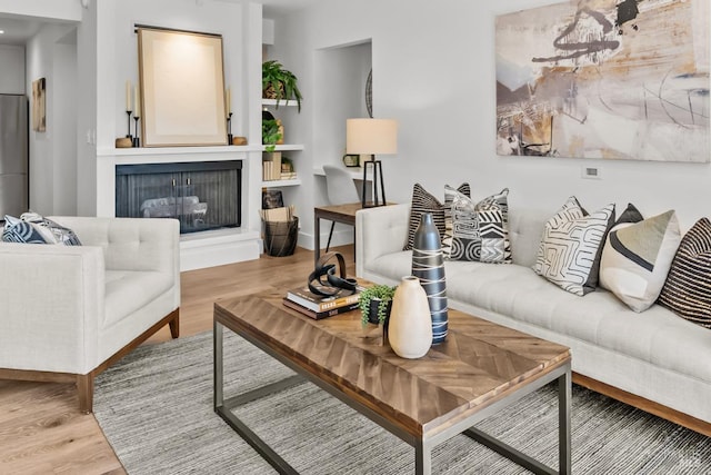 living room featuring baseboards, a fireplace with raised hearth, and wood finished floors