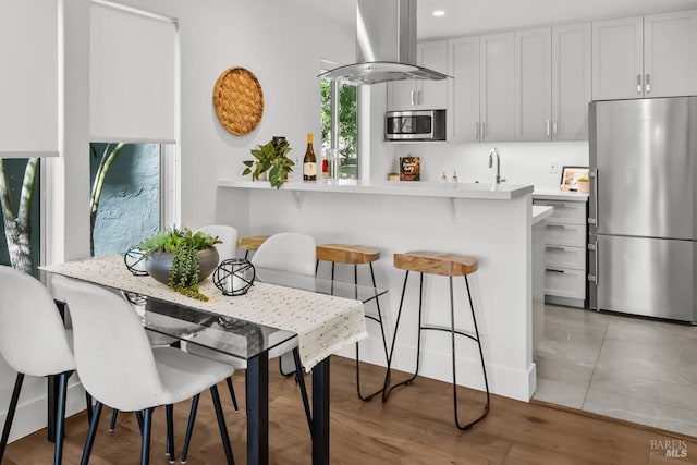 kitchen featuring recessed lighting, a kitchen breakfast bar, ventilation hood, light countertops, and appliances with stainless steel finishes