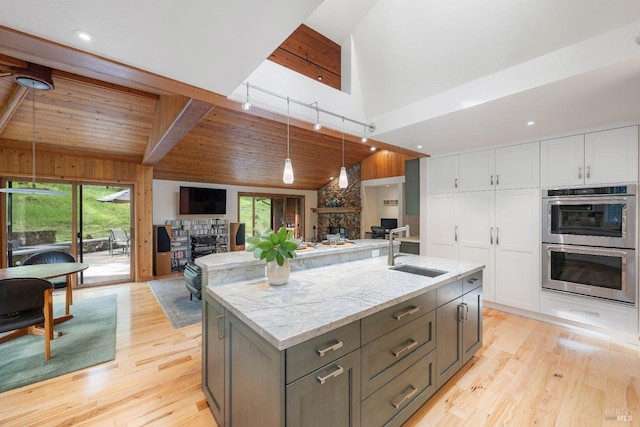 kitchen featuring a sink, double oven, a fireplace, open floor plan, and white cabinets
