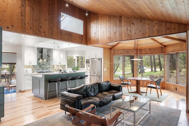 living room with wood walls, light wood-style flooring, high vaulted ceiling, and wood ceiling