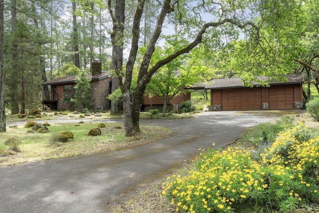 view of front of property with stone siding, a chimney, aphalt driveway, and a detached garage