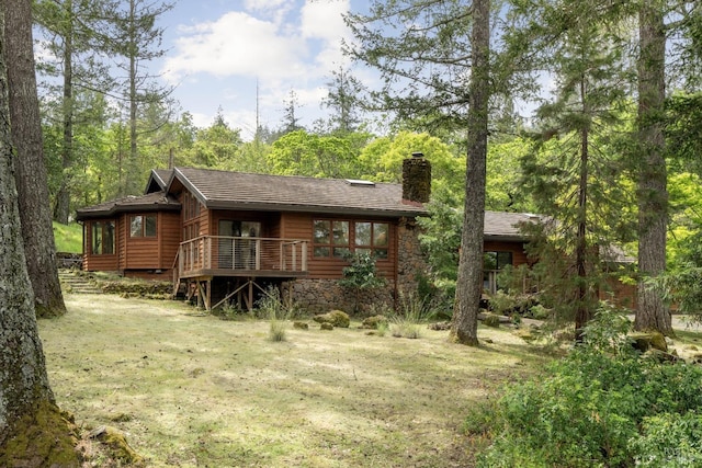 back of house with stone siding, a lawn, a chimney, and a wooden deck