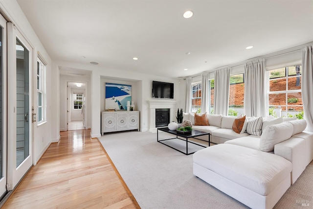 living area with recessed lighting, a healthy amount of sunlight, a glass covered fireplace, and light wood-type flooring