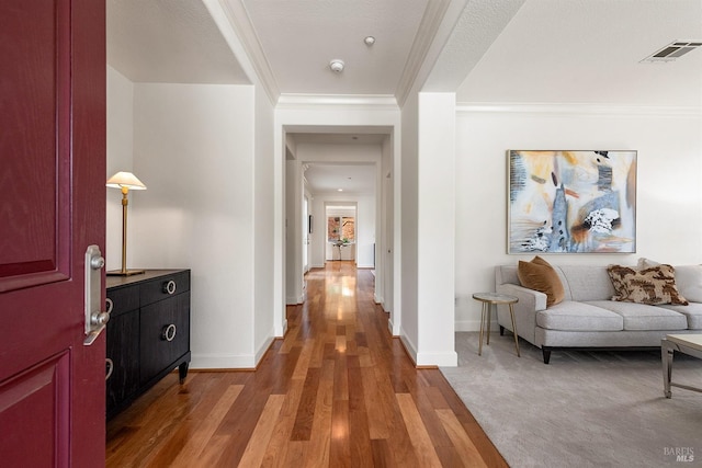 corridor featuring light wood finished floors, crown molding, visible vents, and baseboards