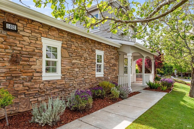 doorway to property with a lawn, stone siding, and covered porch