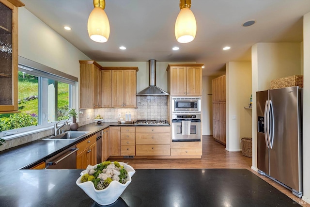 kitchen with a sink, wall chimney range hood, backsplash, dark countertops, and appliances with stainless steel finishes