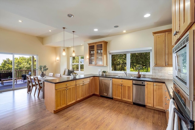 kitchen with a sink, a peninsula, stainless steel appliances, wood finished floors, and plenty of natural light