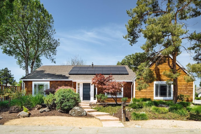 view of front of house featuring roof mounted solar panels and a shingled roof