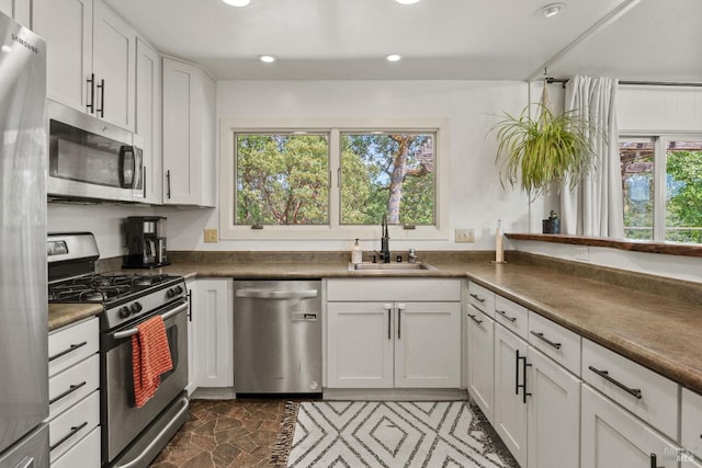 kitchen with a sink, stainless steel appliances, recessed lighting, white cabinetry, and dark countertops