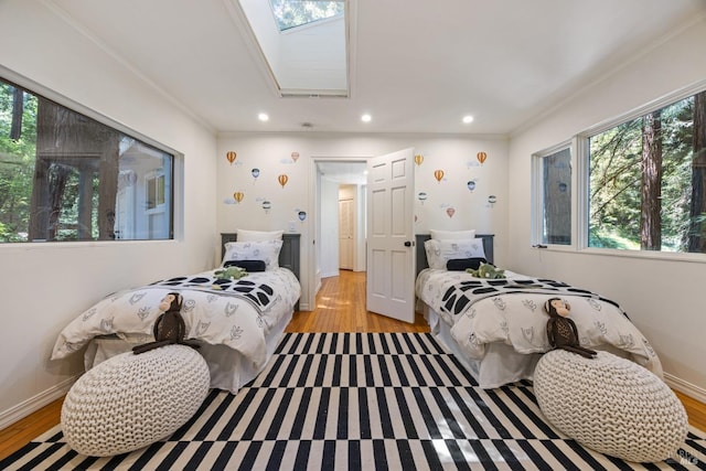 bedroom with multiple windows, light wood-type flooring, and a skylight