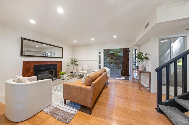 living room with light wood-type flooring, visible vents, a glass covered fireplace, and recessed lighting