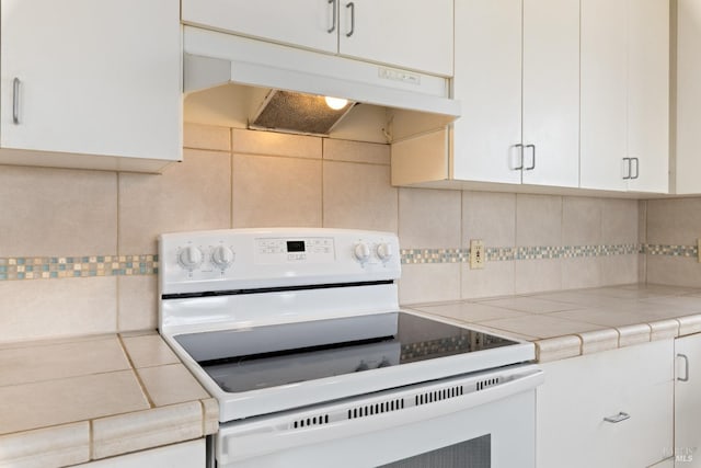 kitchen with under cabinet range hood, white electric stove, backsplash, tile counters, and white cabinets
