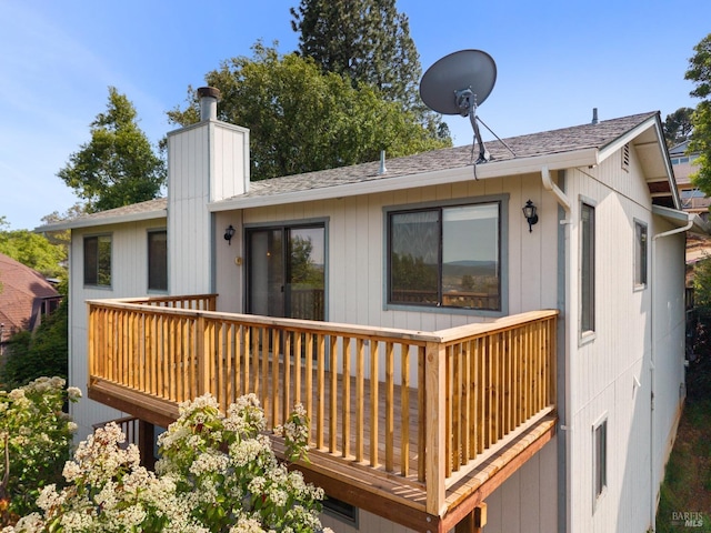 back of property featuring a chimney, a deck, and roof with shingles