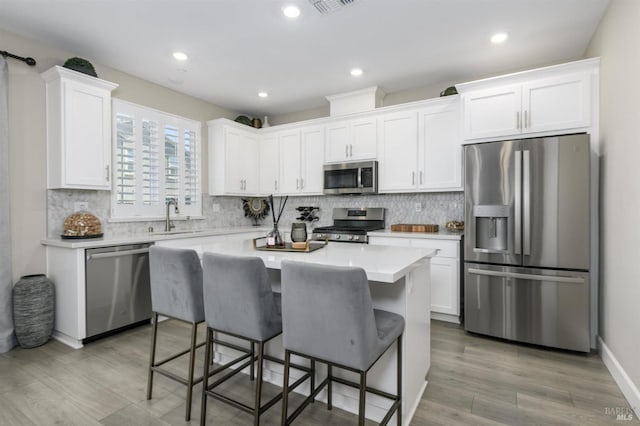 kitchen with stainless steel appliances, a kitchen breakfast bar, white cabinetry, backsplash, and light countertops