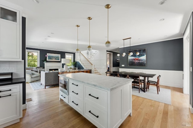 11 Heather Way, Larkspur, CA 94939 - kitchen featuring stainless steel microwave, a warm lit fireplace, crown molding, light wood finished floors, and pendant lighting