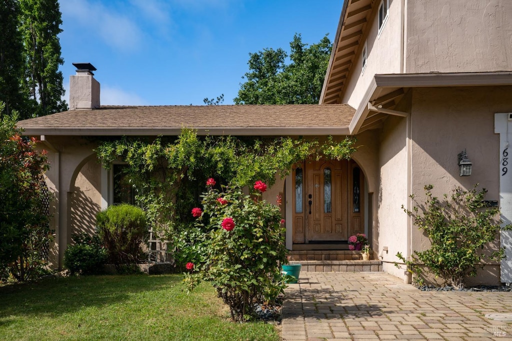 entrance to property featuring a yard, stucco siding, and a chimney