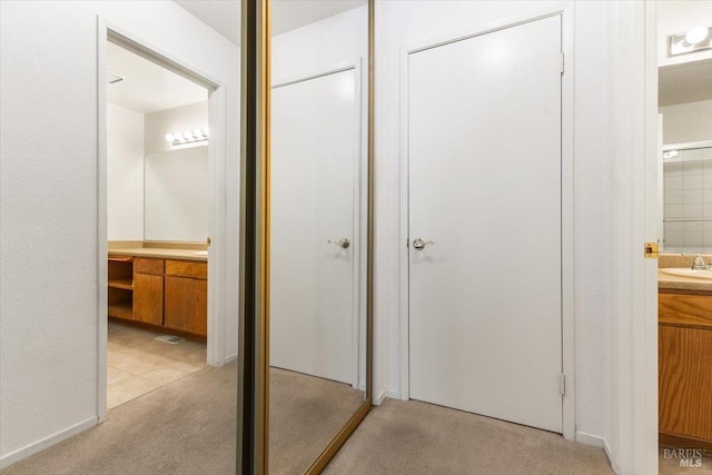 hall with light colored carpet and a sink