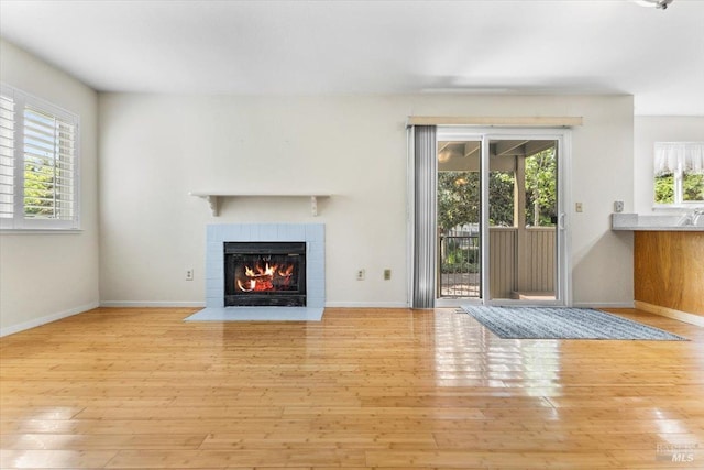unfurnished living room with baseboards, a tiled fireplace, and wood finished floors
