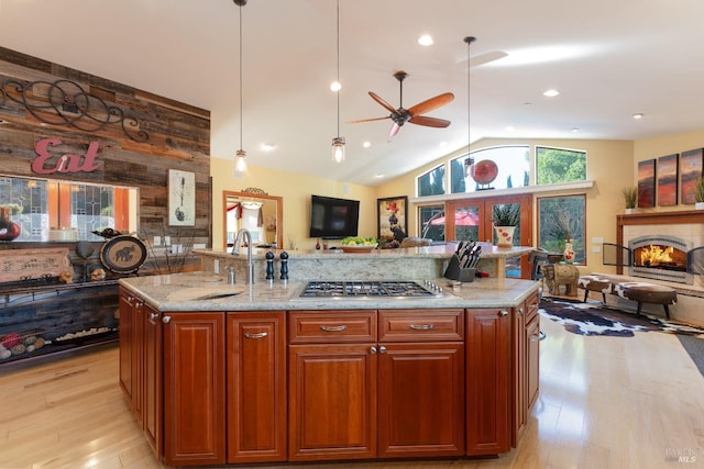 kitchen with a ceiling fan, stainless steel gas cooktop, light wood finished floors, a sink, and open floor plan