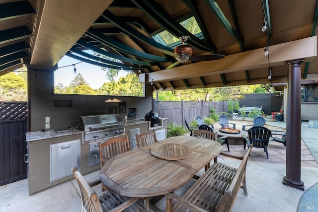 view of patio featuring a ceiling fan, an outdoor kitchen, outdoor dining area, fence, and a fire pit