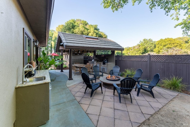 view of patio / terrace featuring a fenced backyard, an outdoor fire pit, a sink, and an outdoor kitchen