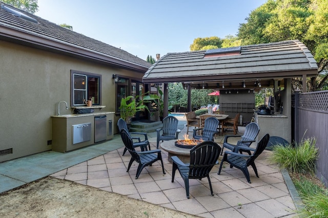 view of patio featuring a gazebo, an outdoor kitchen, a fire pit, and fence