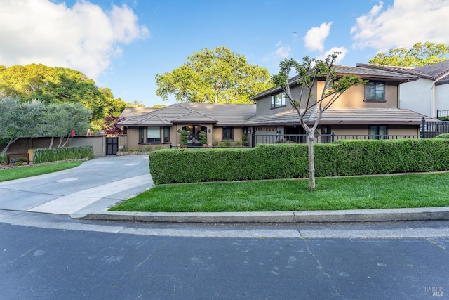 view of front facade with a front lawn, stucco siding, a tile roof, and fence private yard