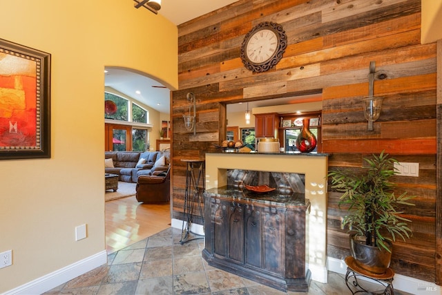 bar featuring high vaulted ceiling, wood walls, arched walkways, and baseboards